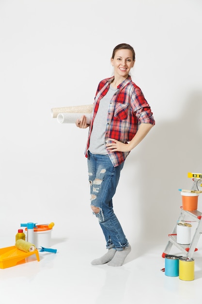 Full length of pretty woman in casual clothes standing near instruments for renovation apartment home isolated on white background. Wallpaper, accessories for gluing, painting tools. Repair concept.