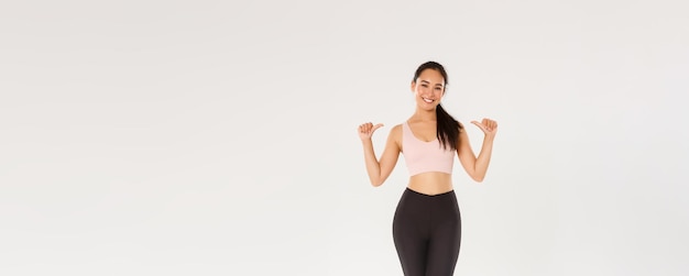 Photo full length of professional fitness coach asian girl athelte pointing at herself and smiling happy w