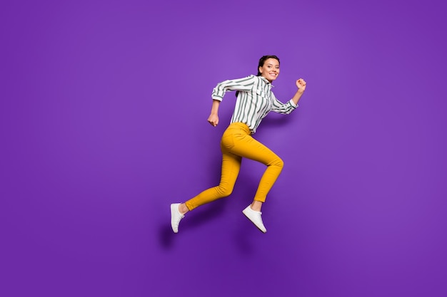 Full length profile photo of crazy beautiful lady jumping high rushing discount prices shopping wear striped shirt yellow trousers isolated purple color background