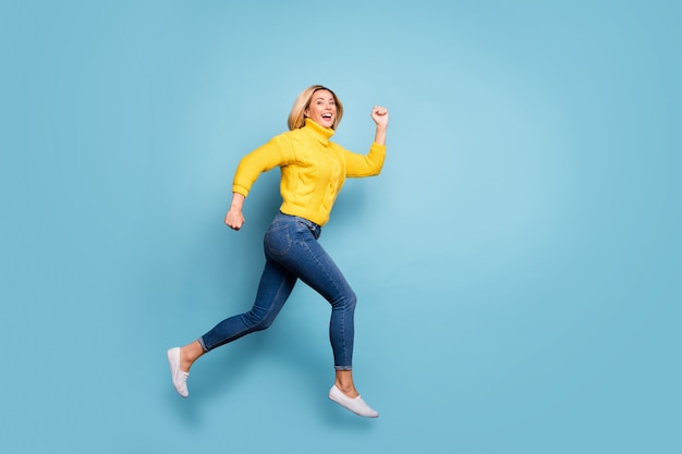 Full length profile photo of crazy lady jumping high rushing shopping center black friday sale wear knitted yellow pullover jeans isolated blue color wall 