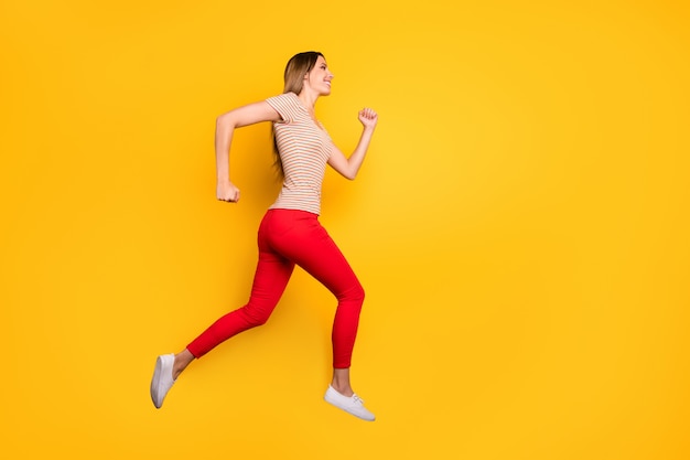 Full length profile photo of funky lady jumping high rushing discount shopping store addicted person wear casual striped t-shirt red trousers isolated yellow color wall