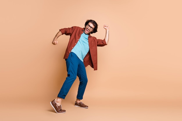 Full length profile photo of guy dance open mouth wear glasses brown t-shirt trousers shoes isolated beige color background