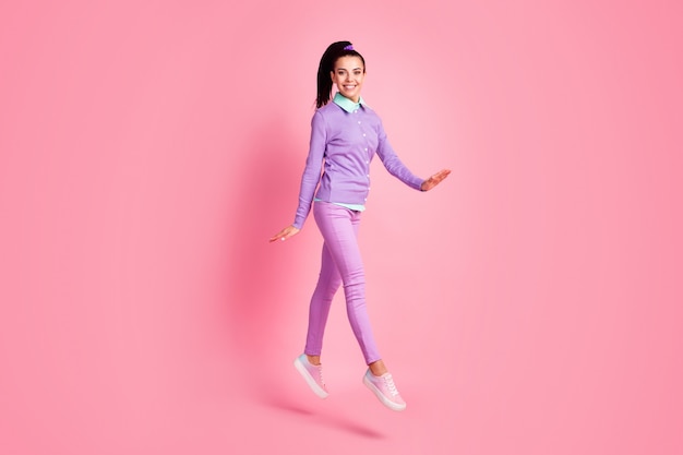 Полная длина фото профиля леди прыжок прогулки девичьи руки носить фиолетовый пуловер брюки кроссовки изолированный розовый цвет фона
