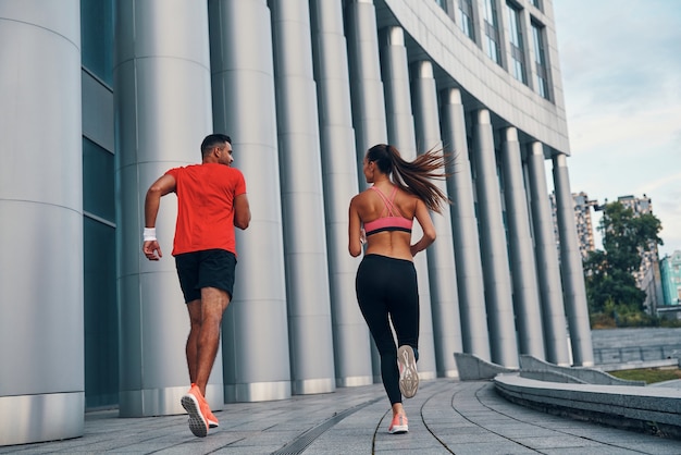 Foto vista posteriore a tutta lunghezza della coppia atletica in abbigliamento sportivo che si gode il jogging mattutino mentre si pratica all'aperto sulla strada della città city
