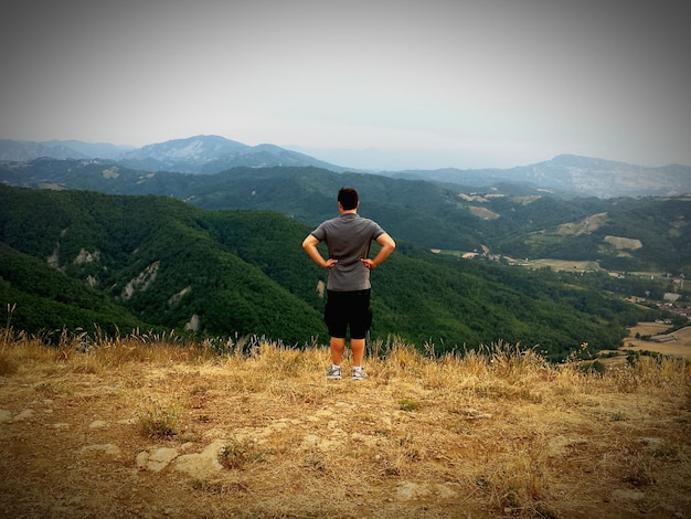 写真 明るい空に照らされた山の前にある丘の上に立っている男の全長の後ろの景色