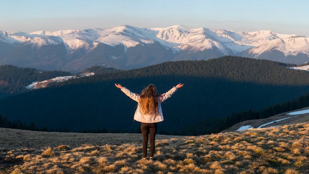 Полный снимок заднего вида авантюрной женщины-путешественницы, стоящей на вершине горы с расставленными руками