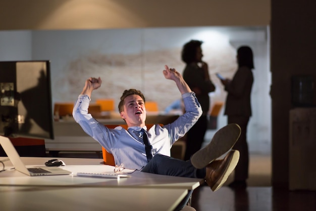 Full length of a relaxed casual young businessman sitting with legs on desk at night office