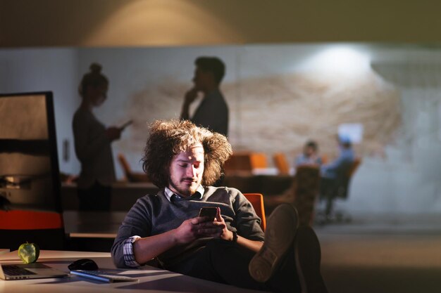 Full length of a relaxed casual young businessman sitting with legs on desk at night office