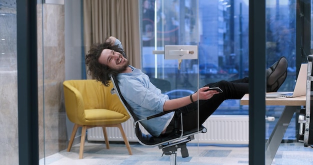 Foto integrale di un giovane uomo d'affari casual rilassato seduto con le gambe sulla scrivania in ufficio