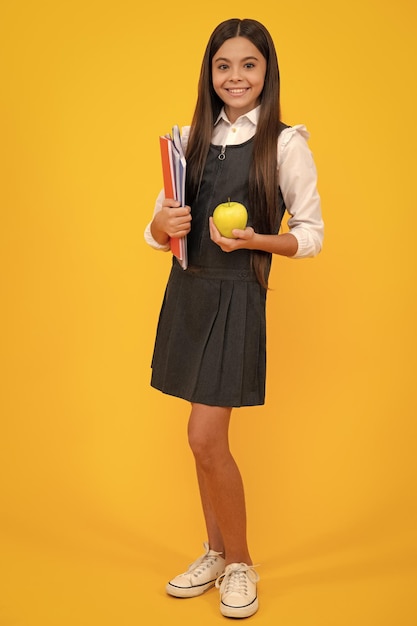 Full length of schoolchild teenage student girl with school bag backpack hold aplle on yellow isolated studio background children school and education concept