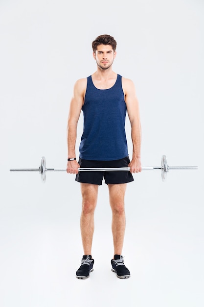 Full length of serious young sportsman exercising with barbell over white background