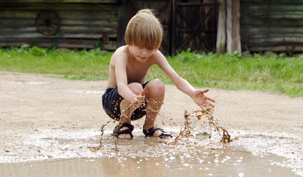 Photo full length of shirtless boy playing with muddy water