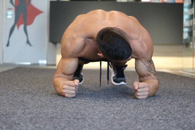 Foto lunghezza intera di un uomo senza camicia che fa flessioni sul pavimento in palestra