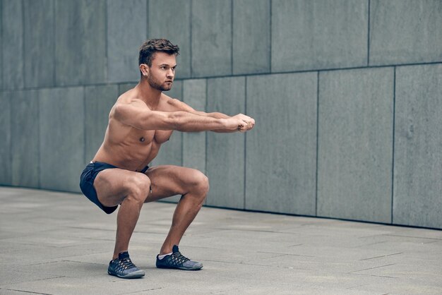 full length of shirtless man exercising on footpath by wall