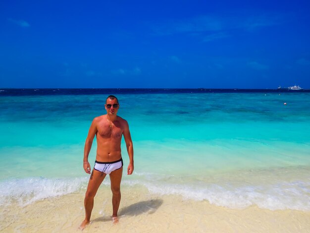 Foto lunghezza completa di un uomo senza camicia in piedi sulla spiaggia contro il cielo