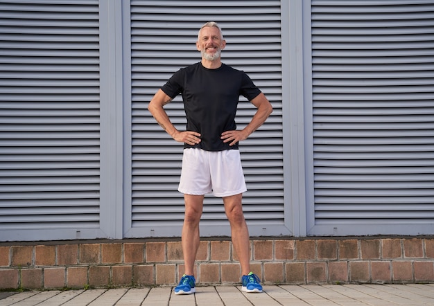 Full length shot of active middle aged man in good shape smiling while standing with arms on waist