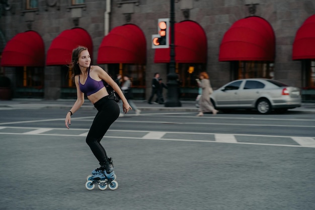 Full length shot of active slim young woman dressed in sportsclothes rides on rollers to strengthen arms and legs muscles improves balance agility and coordination has good mood burns calories