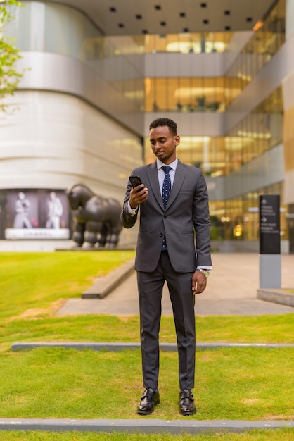 Foto colpo integrale dell'uomo d'affari africano che sta all'aperto facendo uso del telefono