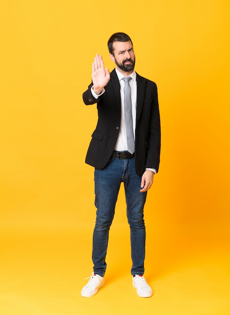 Full-length shot of business man over isolated yellow making stop gesture