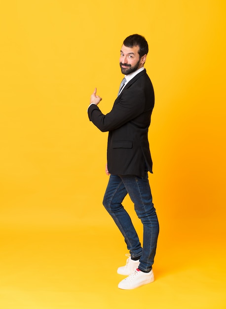 Full-length shot of business man over isolated yellow pointing back