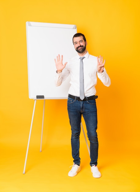 Full-length shot of businessman giving a presentation on white board over isolated yellow counting nine with fingers