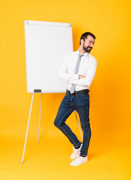 Full-length shot of businessman giving a presentation on white board over isolated yellow wall with arms crossed and happy