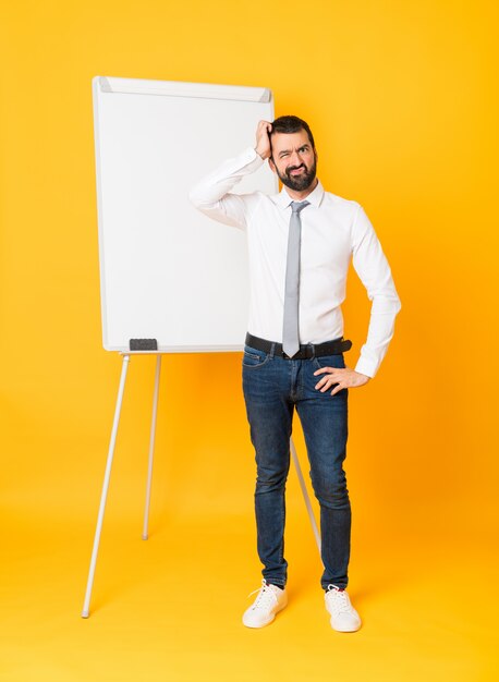 Full-length shot of businessman giving a presentation on white board over isolated yellow with an expression of frustration and not understanding