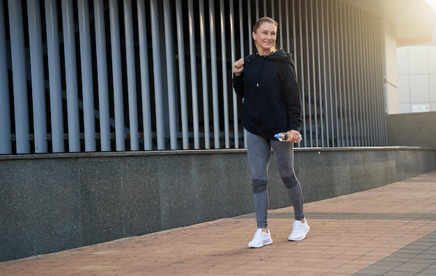 Foto colpo integrale di allegra sportiva di mezza età che sorride via mentre cammina in città pronta