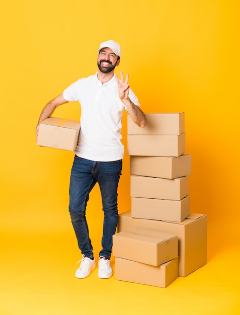 Full-length shot of delivery man among boxes over isolated yellow happy and counting three with fingers