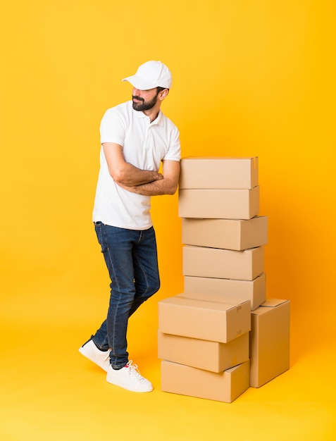 Full-length shot of delivery man among boxes over isolated yellow with arms crossed and happy