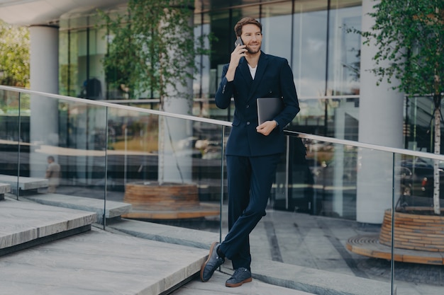 Full length shot of elegant businessman in formal clothes has telephone conversation