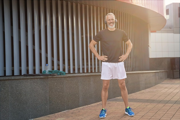 Colpo integrale di gioioso uomo sportivo di mezza età in abbigliamento sportivo e cuffie che sorride mentre