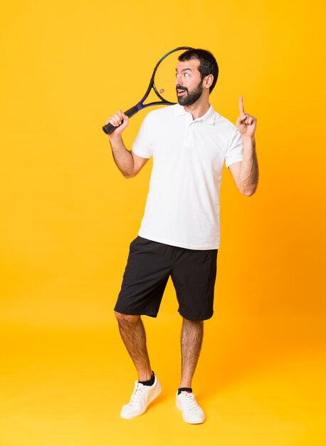 Full-length shot of man over isolated yellow background playing tennis and pointing up