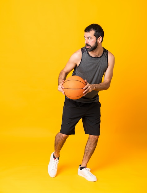 Full-length shot of man over isolated yellow playing basketball