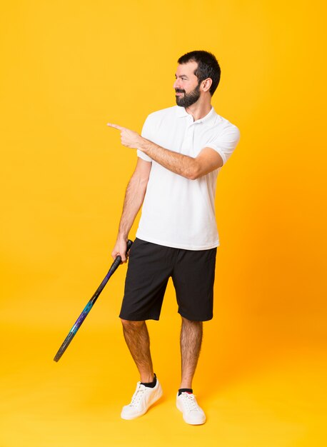 Full-length shot of man over isolated yellow playing tennis and pointing to the lateral