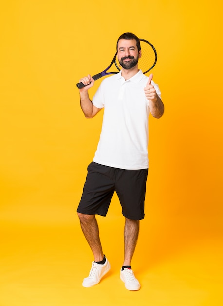 Полнометражный снимок человека над желтым, играя в теннис и с большим пальцем вверх