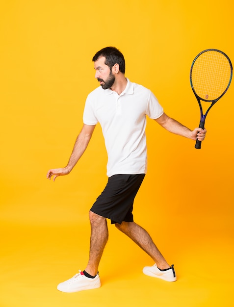Full-length shot of man playing tennis over isolated yellow