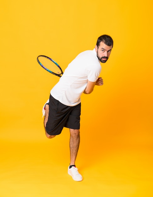 Full-length shot of man playing tennis over isolated yellow 