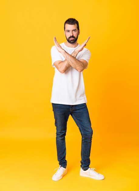 Full-length shot of man with beard over isolated yellow background making NO gesture