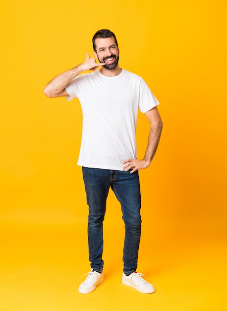 Full-length shot of man with beard over isolated yellow background making phone gesture. Call me back sign