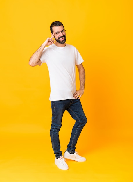 Full-length shot of man with beard over isolated yellow background with glasses and smiling