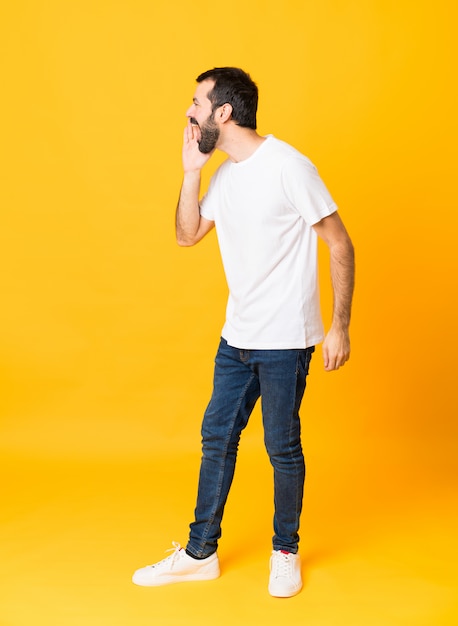 Full-length shot of man with beard over isolated yellow shouting with mouth wide open to the lateral