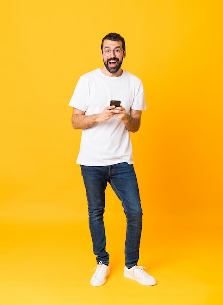 Full-length shot of man with beard over isolated yellow surprised and sending a message