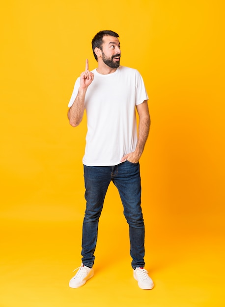 Full-length shot of man with beard over isolated yellow thinking an idea pointing the finger up