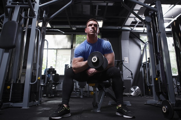 Photo full length shot of a muscular sportsman on weight training at gym doing biceps curls with dumbbell