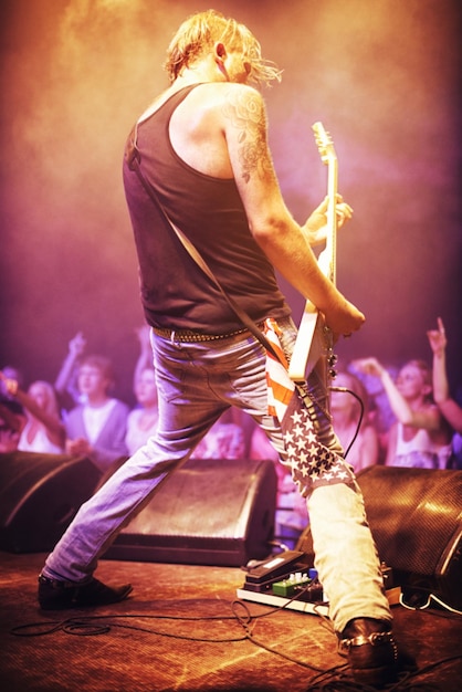 Full length shot of a musician playing guitar for a crowd at a gig