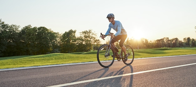 Full length shot of professional male racer in sportswear and helmet training riding road bike