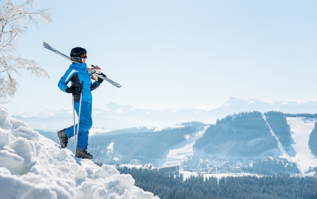 Full length shot van een vrouwelijke skiër die de helling afloopt met haar ski's op de schouder. winterskigebied en bergen