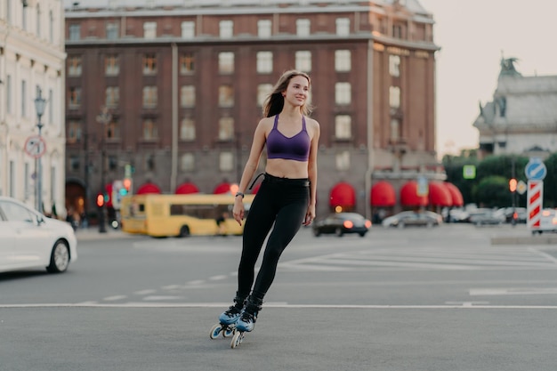 Full-length shot van sportieve slanke vrouw in actieve slijtage ritten op bladen geniet van outdoor fitness activiteit tijdens warme zomerdag poses op stedelijke plaats op asfalt Rollerblading en leisure concept