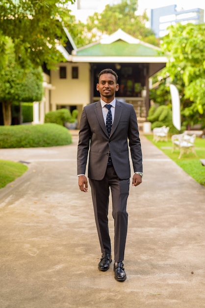 Молодой красивый африканский бизнесмен в полный рост гуляет в парке